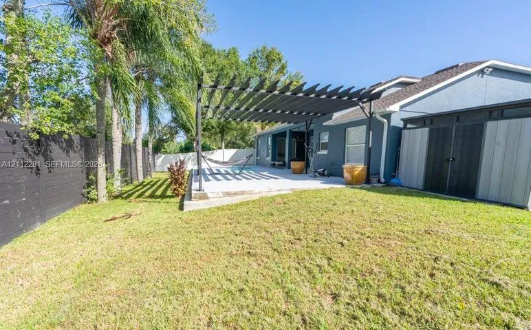 Backyard featuring a concrete patio, black metal pergola, horizontal slat fencing, and mature palm trees