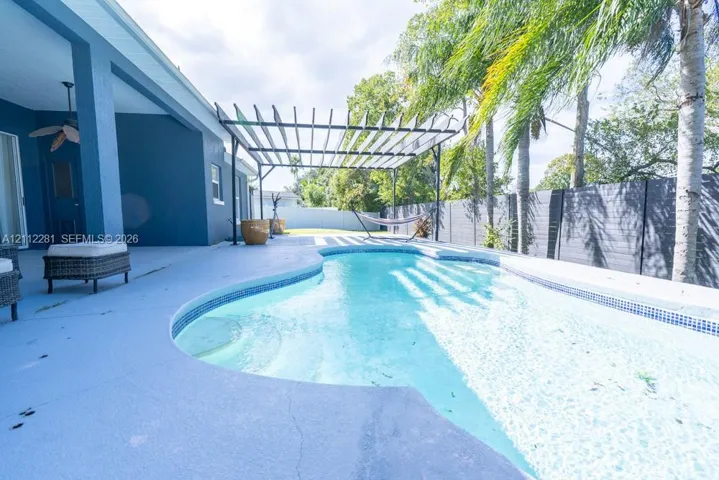 Outdoor living space featuring an in-ground swimming pool, a metal pergola, a covered patio with a ceiling fan, and privacy fencing