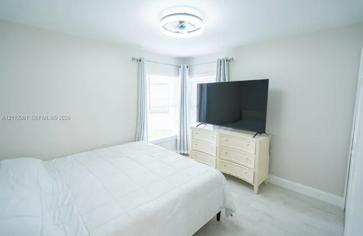 Neutral interior room featuring light-toned wood-finish flooring, dual windows with wall-mounted curtain rods, and a circular LED flush-mount ceiling light