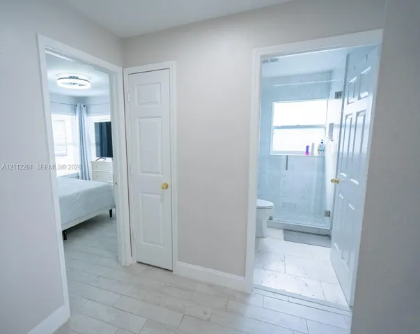 Hallway featuring wood-finish flooring, white panel doors, and entry into a bathroom with tile surround shower