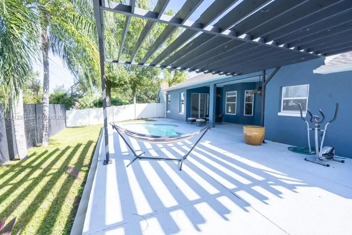 Outdoor patio featuring a dark metal pergola, concrete flooring, in-ground swimming pool, and white perimeter privacy fencing