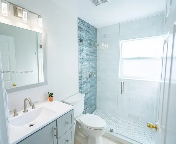 Bathroom featuring a vanity with a white countertop and rectangular undermount sink, a walk-in shower with glass enclosure, textured blue tile accent wall, and three-light brushed-nickel fixture above the mirror