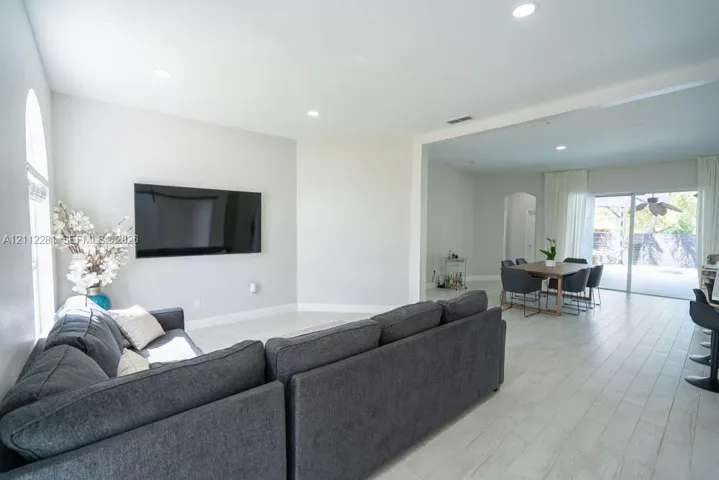 Open-concept interior featuring light-toned tile flooring, recessed ceiling lighting, arched wall detailing, and glass sliding doors