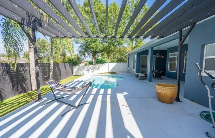 Covered patio with a custom wood-beam pergola, swimming pool, concrete hardscaping, and perimeter fencing