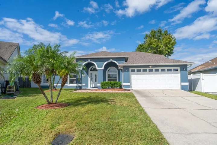 Stucco exterior with arched architectural detailing, decorative entry columns, multi-pane garage door, and manicured landscaping
