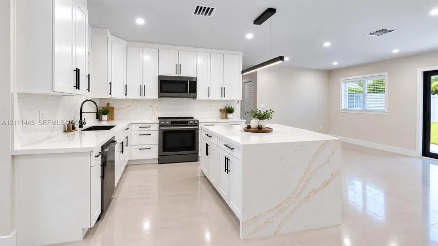 Kitchen featuring white shaker-style cabinetry, a large central island with waterfall-edge countertop, stone-surfaced backsplash, recessed lighting, and built-in stainless steel appliances