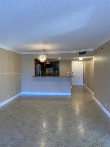 Open-concept area featuring stone-finish floor tiling, crown molding, a decorative multi-bulb chandelier, and a kitchen pass-through breakfast bar