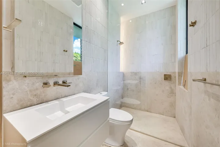 Floating vanity with integrated sink and wall-mounted faucet, walk-in shower with glass partition, floor-to-ceiling tiled walls, and recessed lighting