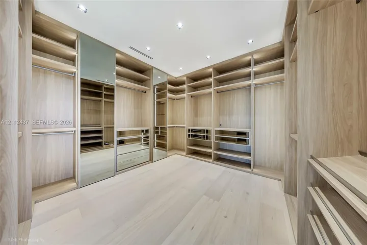 Custom built-in wood-finish cabinetry featuring extensive shelving, hanging rods, integrated mirrors, and recessed ceiling lighting throughout