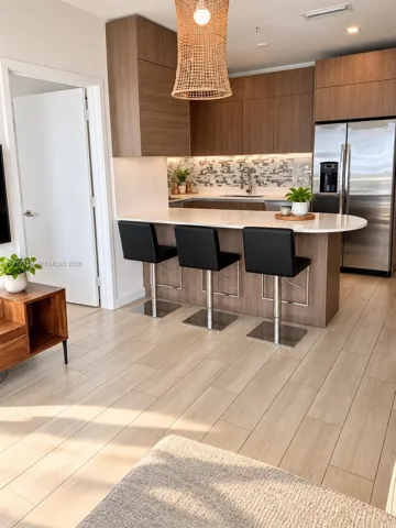 Kitchen featuring flat-panel wood-finish cabinetry, quartz countertops, mosaic tile backsplash, stainless steel appliances, and wood-finish flooring