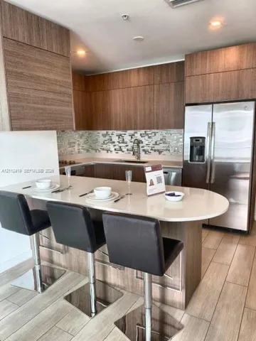 Kitchen featuring flat-panel wood-finish cabinetry, quartz countertops, a mosaic tile backsplash, stainless steel appliances, and wood-finish flooring