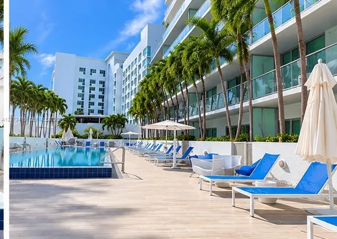 Swimming pool featuring a raised tiled edge, extensive paved pool deck, glass balcony railings, and mature palm trees