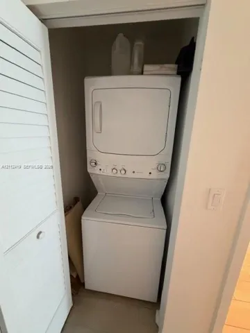 Laundry closet featuring a white stacked washer and dryer unit concealed behind a louvered bi-fold door
