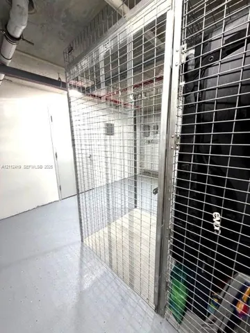 Secure storage unit featuring metal mesh walls, a locking door mechanism, and painted concrete flooring