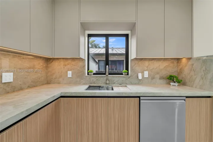 Flat-panel cabinetry with light wood grain finish, integrated stainless steel appliances, stone countertop, full-height stone backsplash, and undermount sink with a pull-down faucet