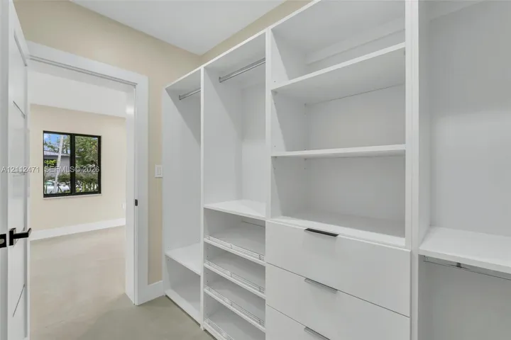 Custom walk-in closet featuring white built-in shelving, integrated garment rods, tiered drawer storage, and matte black hardware