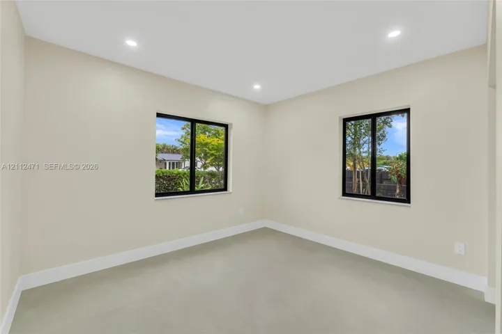 Interior space featuring neutral-toned walls, recessed lighting, dual windows with dark frames, and uniform hard-surface flooring