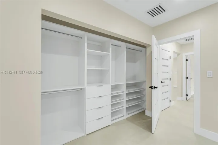 Custom built-in closet featuring floor-to-ceiling white shelving, integrated drawers, pull-out storage racks, and dual hanging rods