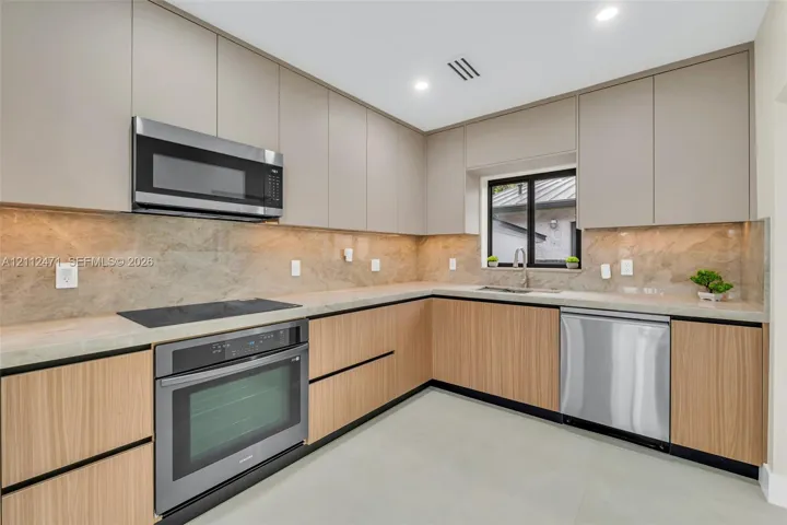 Kitchen featuring two-tone flat-panel cabinetry, stone-finish slab backsplash, stainless steel appliances, integrated cooktop, and neutral countertops
