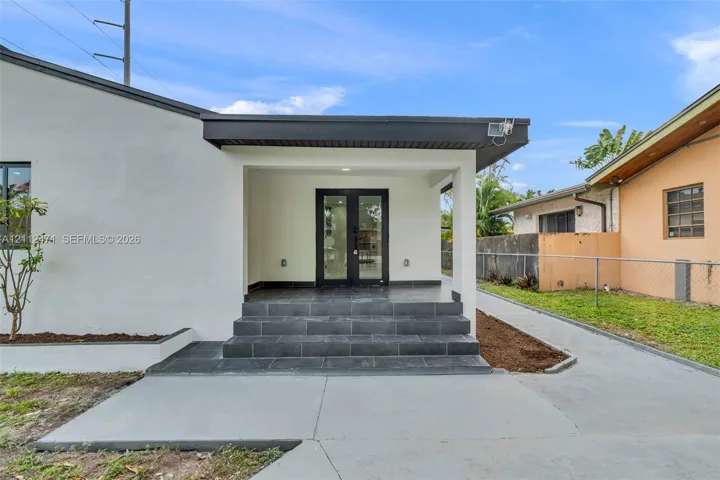 Covered entryway featuring a concrete stoop with dark stone-finish tiling, dual glass-paneled entry doors, and a concrete driveway