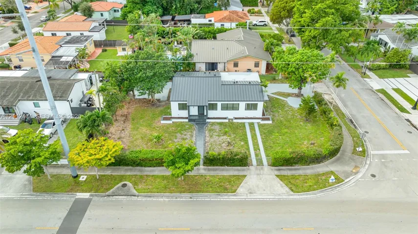 Corner lot residence featuring a standing-seam metal roof, white exterior siding, manicured hedges, and dual concrete driveway strips