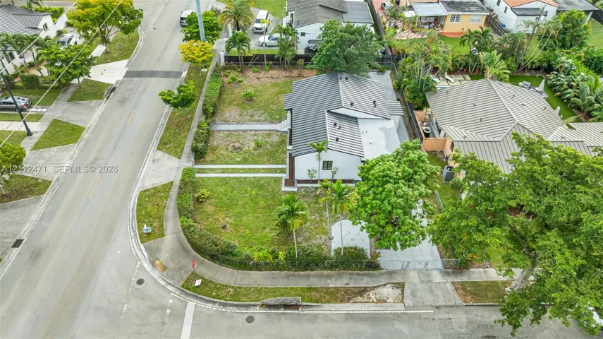 Corner lot residence featuring a standing seam metal roof, paved driveway, and established perimeter landscaping