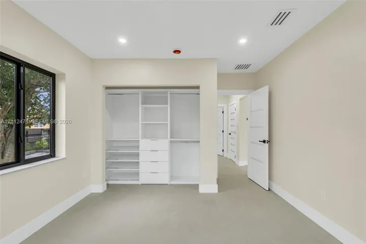 Bedroom featuring recessed lighting, a window with black trim, and a built-in closet system with shelving and drawers