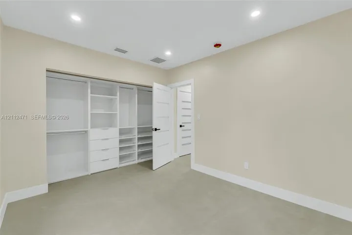 Customized walk-in closet featuring floor-to-ceiling white cabinetry, integrated drawer storage, and multiple shelving units, complemented by solid-core interior doors with matte black hardware and recessed lighting