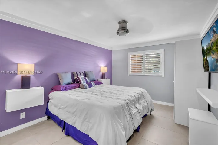 Room featuring neutral tile flooring, wall-mounted floating shelves, crown molding, a ceiling fan, and window shutters