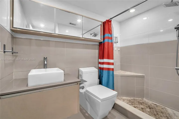 Bathroom featuring a floating vanity with a rectangular vessel sink, wall-mounted mirrored cabinetry, a walk-in shower with a built-in bench, and stone-finish wall tiling