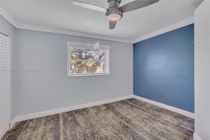 Room featuring an accent wall, crown molding, louvered closet doors, and a ceiling fan with integrated lighting