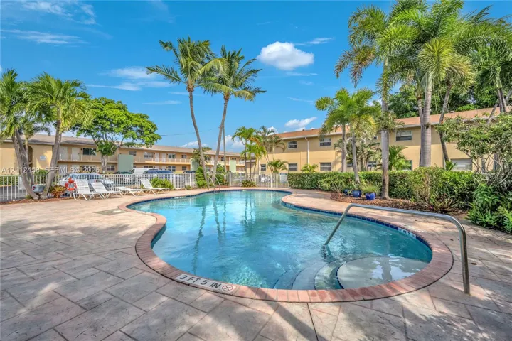 In-ground swimming pool featuring a curved concrete deck, integrated entry steps, and metal safety handrail, surrounded by mature palm trees and landscaping