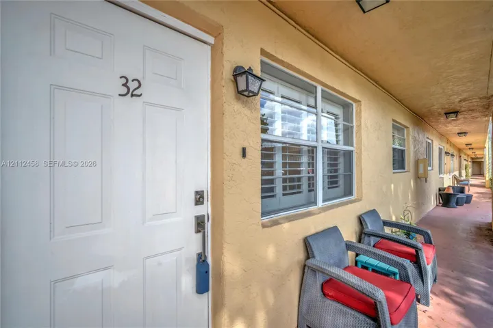 Exterior entry featuring a white six-panel door, metal hardware, a wall-mounted lantern-style light fixture, and window shutters