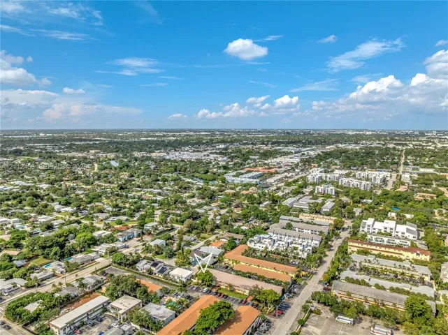 Aerial perspective of a multi-unit residential complex featuring low-rise buildings, terracotta-toned roofing, paved parking areas, and mature landscape trees