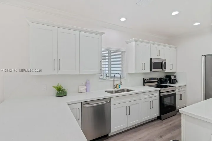 Kitchen featuring white shaker-style cabinetry, solid-surface countertops, recessed lighting, and stainless steel appliances, including an over-the-range microwave and integrated dishwasher, complemented by wood-finish flooring