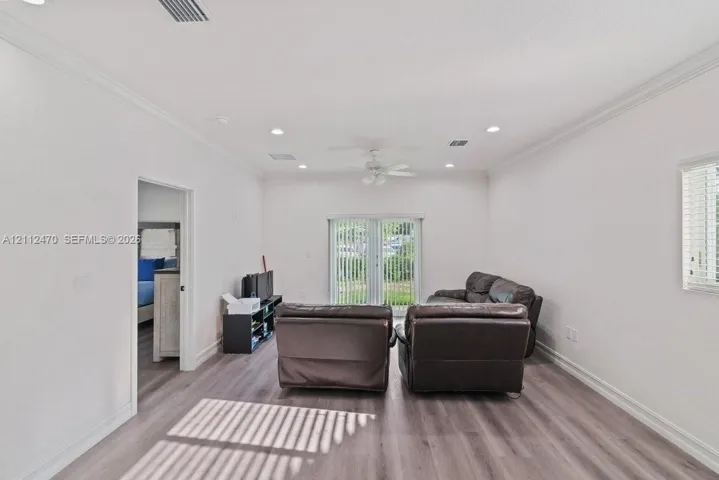 Living area featuring wood-finish flooring, recessed lighting, crown molding, a ceiling fan, and sliding glass doors with vertical blinds