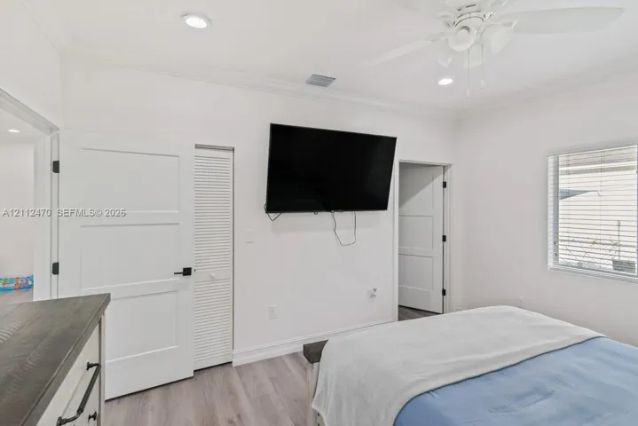 Room featuring recessed lighting, wood-finish flooring, crown molding, a ceiling fan, and louvered closet doors