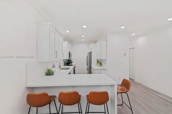 Kitchen featuring white cabinetry, solid-surface countertops, recessed ceiling lighting, and wood-finish flooring