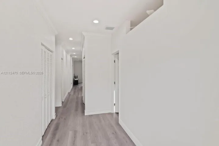 Hallway featuring wood-finish flooring, recessed lighting, and louvered-door closets