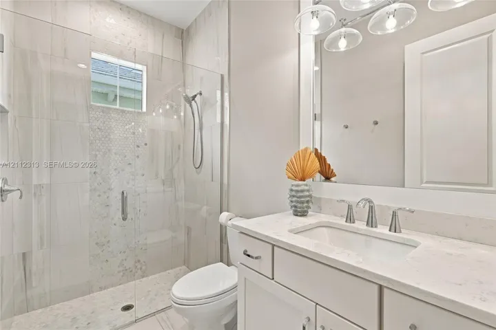 Bathroom featuring a vanity with a white countertop and undermount sink, a walk-in shower with a glass enclosure, floor-to-ceiling tilework, and a multi-bulb light fixture
