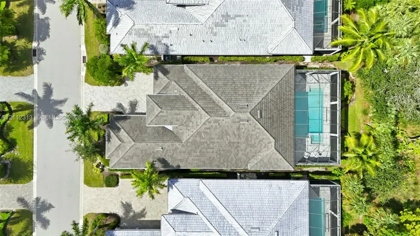 Aerial perspective featuring a multi-hipped roofline, paved driveway, and a screened-in pool enclosure