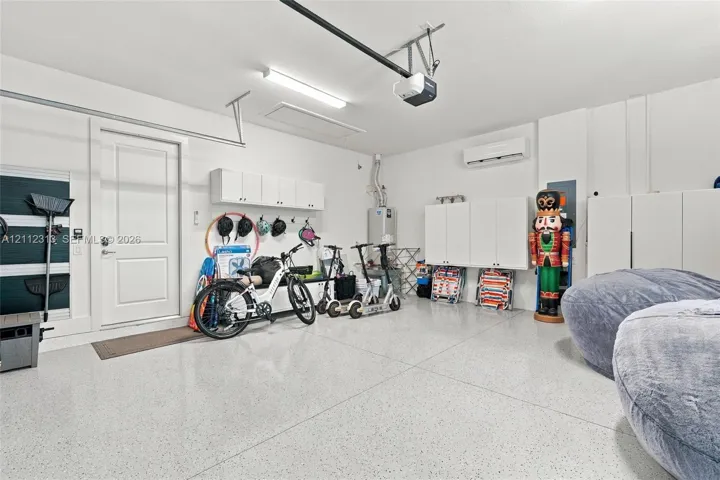 Garage featuring epoxy-coated flooring, wall-mounted white storage cabinetry, an installed climate control unit, and an automated garage door opener system