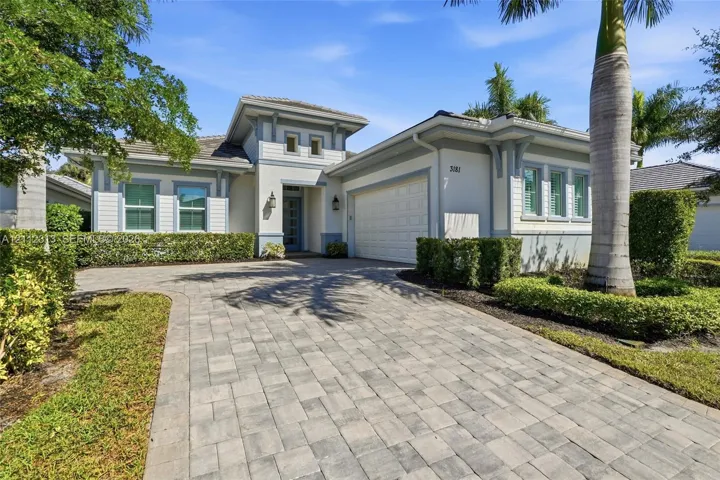 Single-story residence featuring a neutral stucco exterior, paver driveway, multi-pane windows, and a multi-tiered roofline with decorative corbels