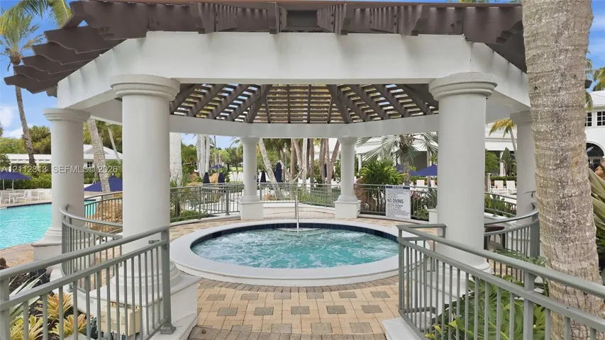 Outdoor gazebo featuring a circular in-ground spa, decorative columns, timber-frame roof structure, and paved stone surround