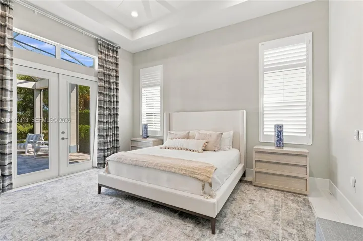 Tray ceiling with recessed lighting, floor-to-ceiling glass French doors, transom windows, and white plantation shutters