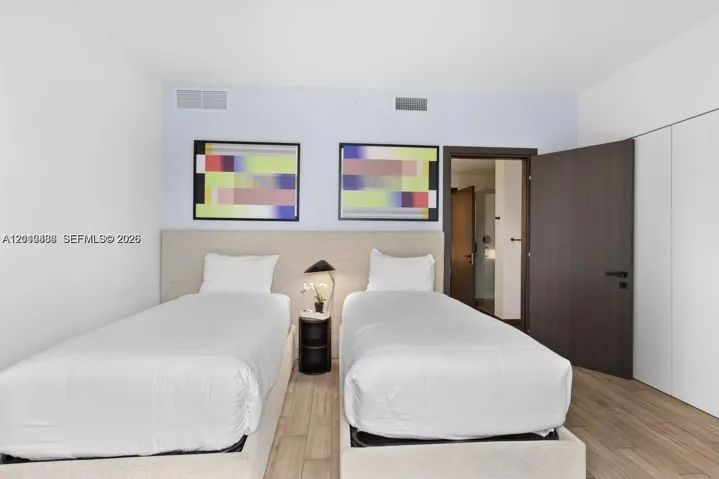 Neutral-toned upholstered headboard with integrated nightstand, wood-finish flooring, and dark-finished solid core swing door