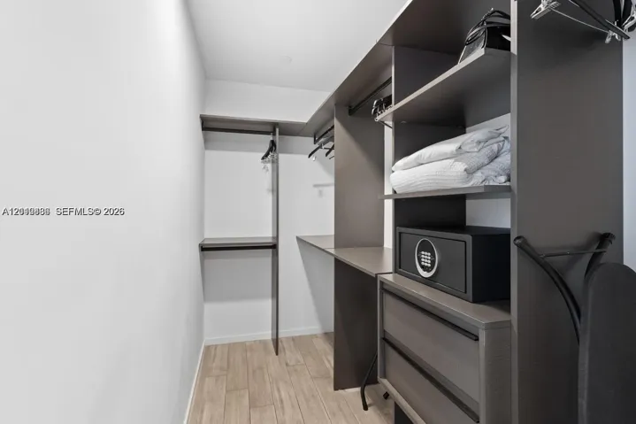 Custom closet system featuring dark wood-finish cabinetry, integrated shelving, hanging rods, and two soft-close drawers, complemented by wood-finish flooring