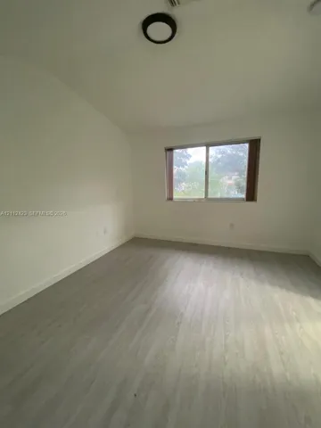 Room interior featuring light-toned wood-finish flooring, neutral walls, a single horizontal window, and a circular flush-mount ceiling light fixture
