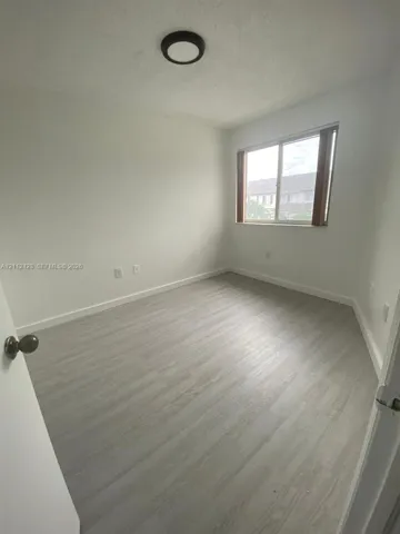 Room featuring light-toned wood-finish flooring, a sliding window with neutral trim, and a low-profile flush-mount ceiling light