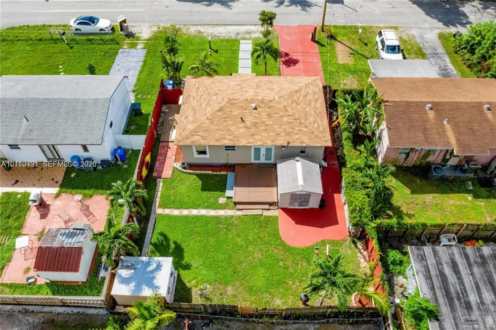Aerial perspective of a property featuring a hip roof, exterior deck, paved driveway, enclosed backyard, and mature palm trees